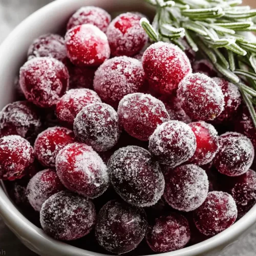 Irresistible Cranberry Candies 2 Close-up of festive sugared cranberries, resembling cranberry candy, in a white bowl with a sugared rosemary sprig.