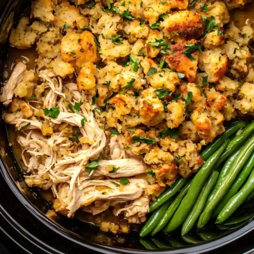 Delicious Crockpot Chicken and Stuffing 2 A close-up of a creamy, golden-brown crockpot chicken and stuffing from a dark dish, garnished with green herbs.