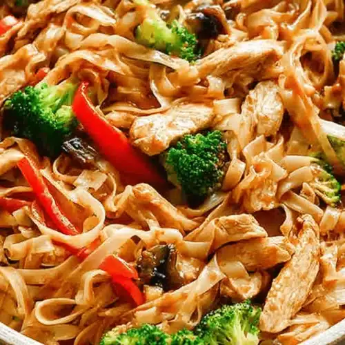 Flavorful Chicken Stir Fry with Noodles 2 A close-up of a rustic bowl filled with chicken stir fry with noodles, vibrant broccoli, red peppers, and mushrooms coated in a rich brown sauce.