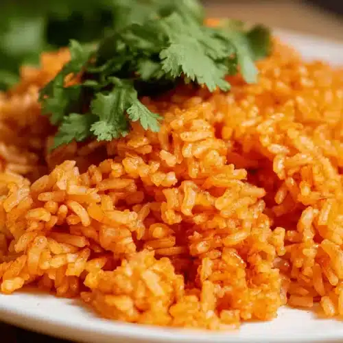 The Best Restaurant-Style Spanish Rice Recipe 2 Close-up of vibrant reddish-orange spanish rice garnished with fresh green cilantro on a white plate.