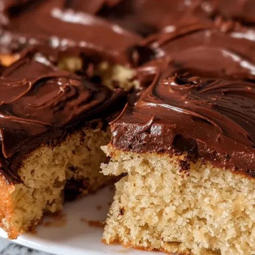 Chocolate Chip Oat Flour Cake 2 Close-up of a delicious slice of Chocolate Chip Oat Flour Cake, generously covered in rich dark chocolate frosting on a white plate.