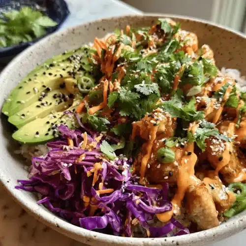 Delicious Bang Bang Chicken Bowls Recipe 2 A vibrant bang bang chicken bowl with crispy chicken, creamy sauce, avocado, and purple cabbage, garnished with sesame seeds and cilantro on a marble surface.