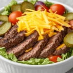 How much protein is in a burger bowl? A classic beef burger bowl with lean grilled beef patties, fresh lettuce, cherry tomatoes, red onions, pickles, shredded cheddar cheese, and light dressing, served in a white ceramic bowl on a rustic wooden table.