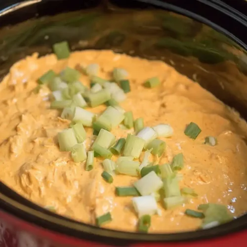 Close-up of a creamy buffalo chicken dip crock pot, garnished with fresh green onions.