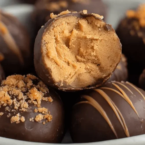 Chocolate-covered Butterfinger Balls with creamy filling, drizzled with caramel and topped with crumbles in a light bowl.