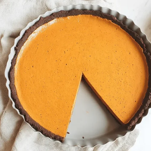 Overhead view of a freshly baked Dark Chocolate Pumpkin Tart with a slice removed, showcasing its rich crust and vibrant filling.