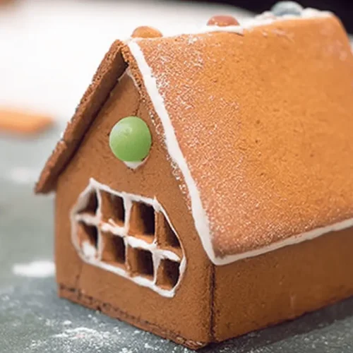 A beautifully decorated gingerbread house with white icing, colorful candies, and powdered sugar.