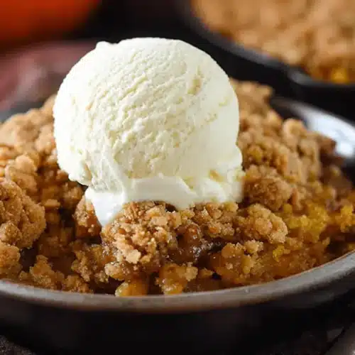 Warm Pumpkin Pie Crisp with melting vanilla ice cream in a rustic bowl, perfect for fall.
