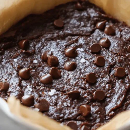 Close-up of fudgy sweet potato brownie recipe with melted chocolate chips and sea salt in a parchment-lined baking dish.