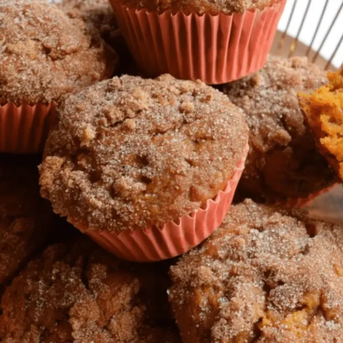 Freshly baked sweet potato muffins with streusel topping, one broken to show its moist, orange interior, illustrating a delicious sweet potato muffin recipe.