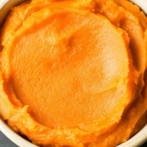 Vibrant sweet potato puree in a rustic beige bowl, presented from an overhead view.