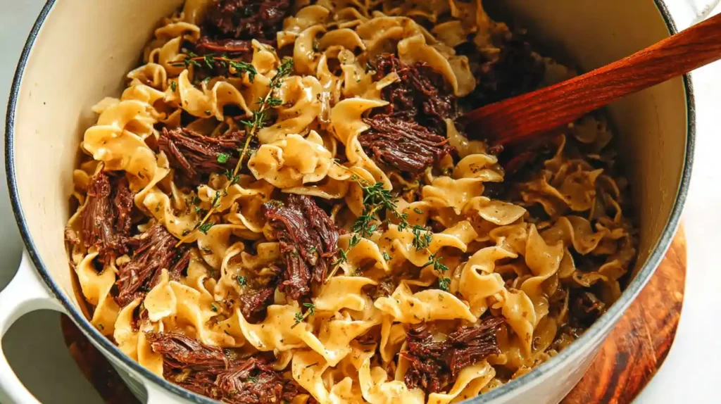 Tender beef and noodles in a creamy savory sauce with shredded beef mixed into egg noodles, served in a large pot.