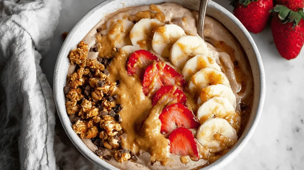 Vibrant Fluffy Protein Yogurt Bowl overhead, topped with granola, chocolate, nut butter, strawberries, and bananas on marble.