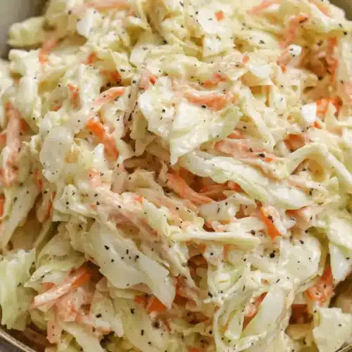 Close-up of a vibrant, creamy classic coleslaw recipe in a rustic ceramic bowl, featuring shredded cabbage and carrots.