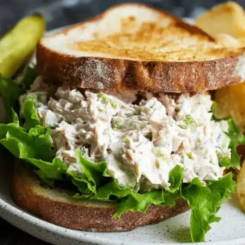 A delicious tuna salad sandwich on toasted bread with a pickle and chips, perfect for a classic tuna salad recipe.